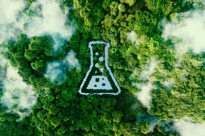Aerial view of a misty green forest with a white laboratory flask shape at its center.
