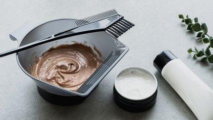Bowl of mixed brown hair dye with a tint brush, alongside hair care products on a countertop.