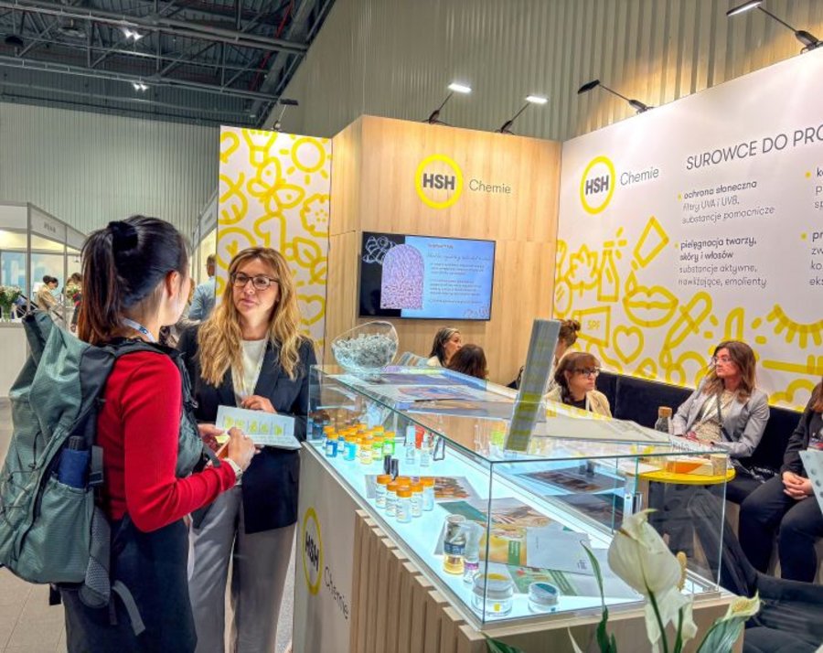 HSH Chemie representative discusses cosmetic samples with a visitor beside booth display cases at PCI Days 2026.