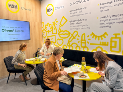 Visitors review sun care documents at yellow tables in the HSH Chemie booth during PCI Days 2026.