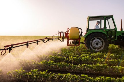 Green tractor spraying plant protection products across field crops in a cultivated agricultural field.