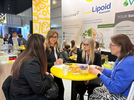 Four women talk at a yellow table with product samples in front of the Lipoid Kosmetik display at HPCI 2026 in Warsaw.