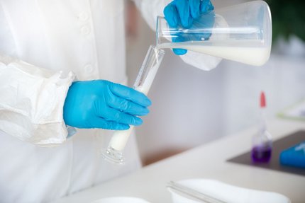 Lab technician in gloves pouring milk into a test tube to test lactase enzyme activity.